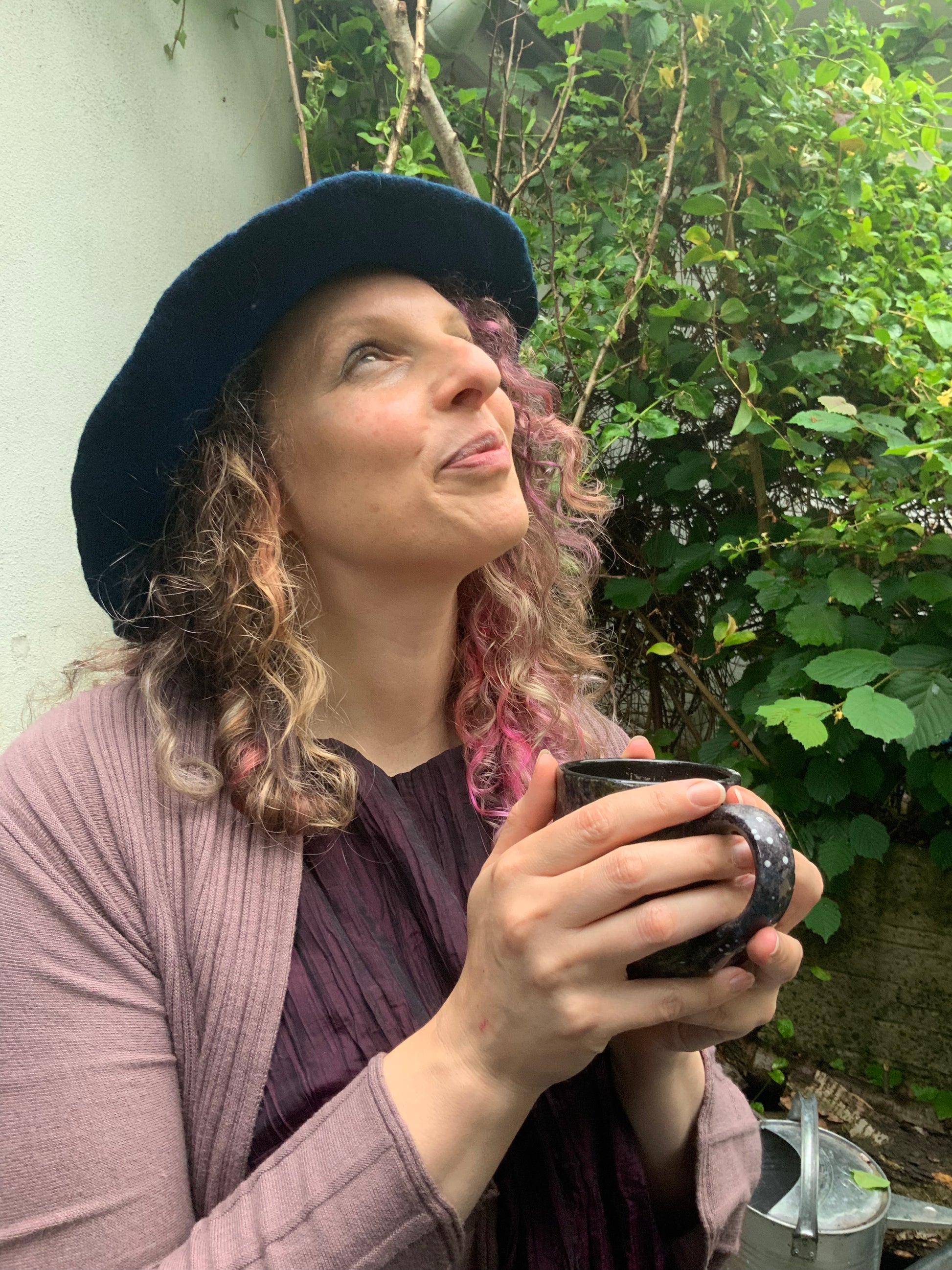 Sam sits in her garden in summer with a witchy hat and cup of tea